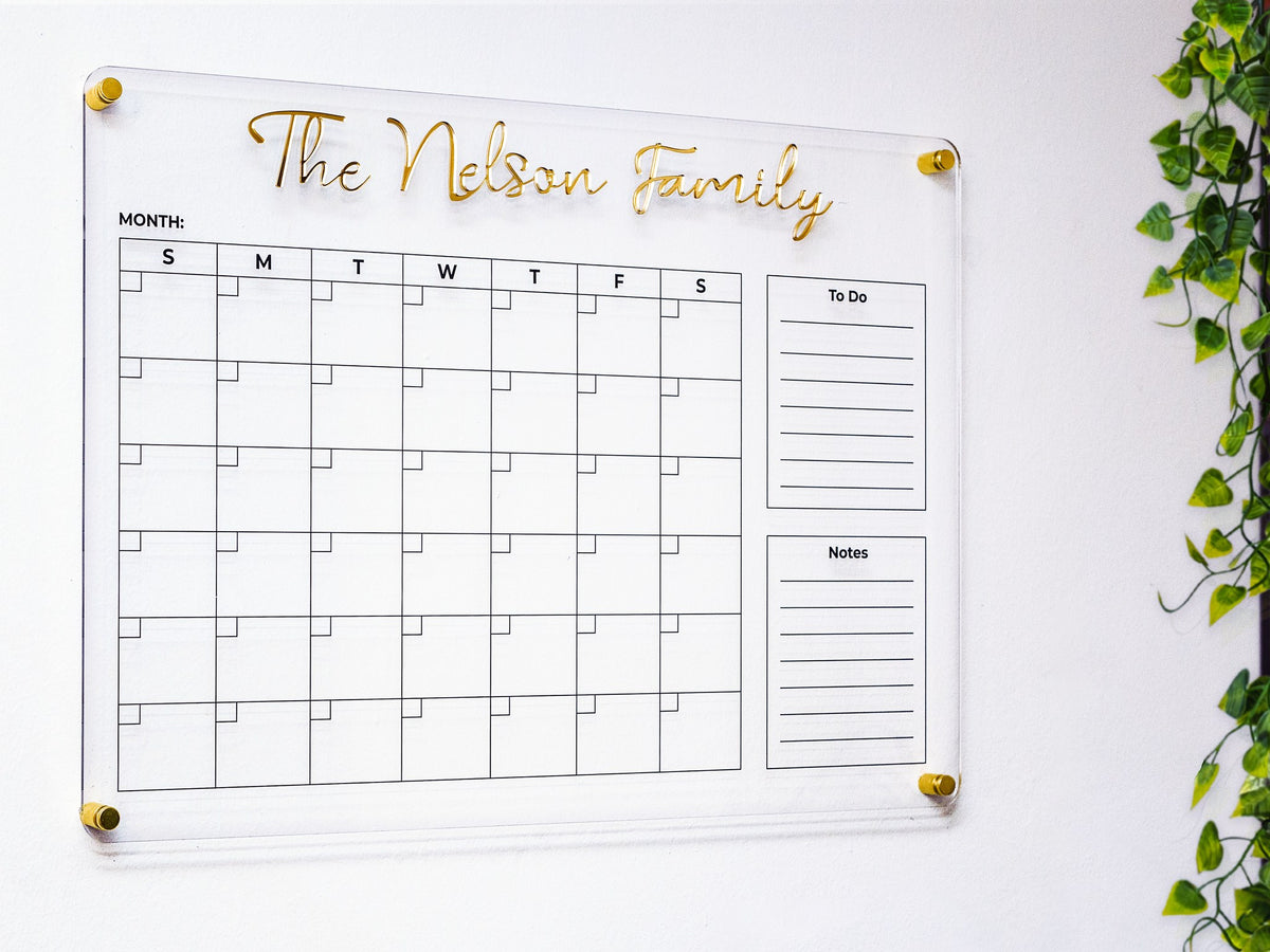 Personalized acrylic family planner with 3D gold name letters on a white wall