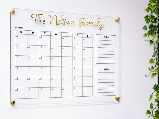 Personalized acrylic family planner with 3D gold name letters on a white wall