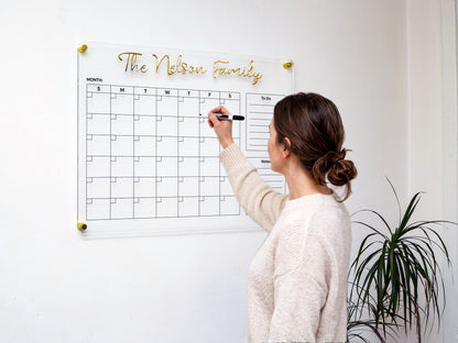 Woman writing on a personalized acrylic family planner with gold 3D name letters