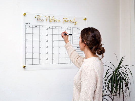 Woman writing on a personalized acrylic family planner with gold 3D name letters